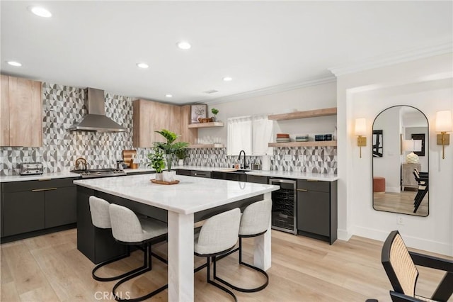 kitchen featuring wine cooler, a breakfast bar, gray cabinetry, a center island, and wall chimney range hood