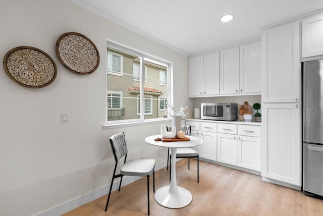 kitchen with stainless steel appliances, white cabinetry, ornamental molding, and light wood-type flooring