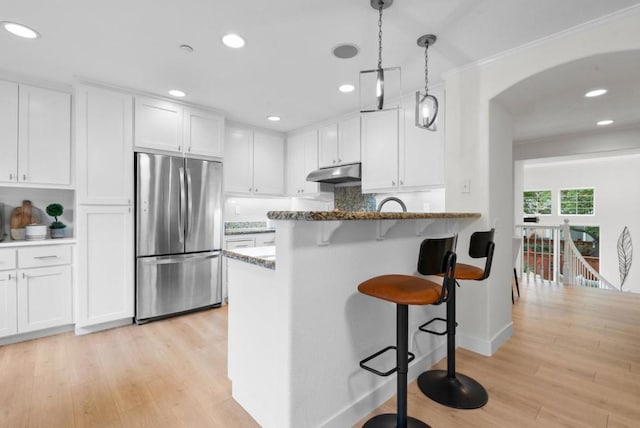 kitchen with stainless steel refrigerator, white cabinetry, dark stone counters, and a breakfast bar