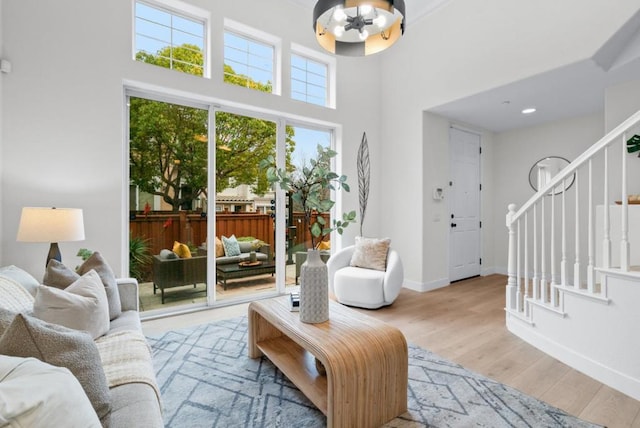 living room with a towering ceiling, a chandelier, and light hardwood / wood-style floors