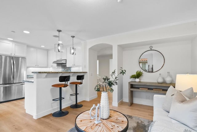 kitchen with a breakfast bar area, dark stone countertops, white cabinets, built in refrigerator, and hanging light fixtures