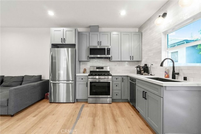 kitchen featuring sink, gray cabinetry, light hardwood / wood-style flooring, appliances with stainless steel finishes, and decorative backsplash