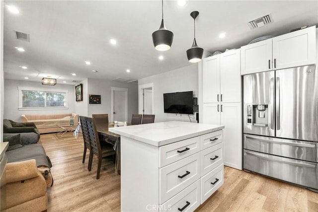 kitchen featuring light stone counters, stainless steel fridge with ice dispenser, hanging light fixtures, light wood-type flooring, and white cabinets