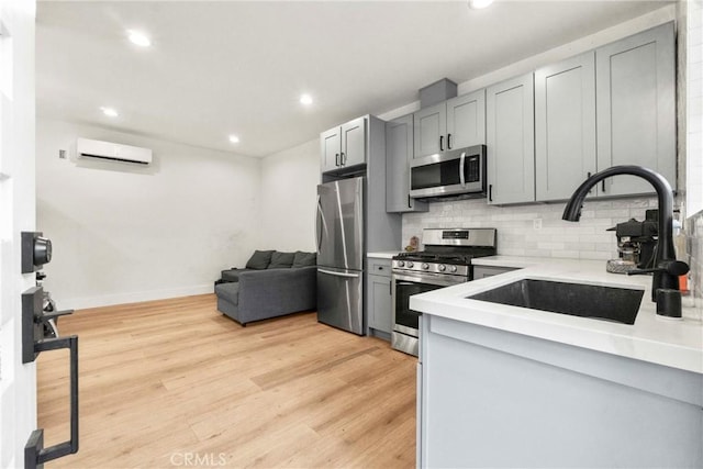 kitchen featuring sink, a wall mounted AC, light wood-type flooring, appliances with stainless steel finishes, and gray cabinets