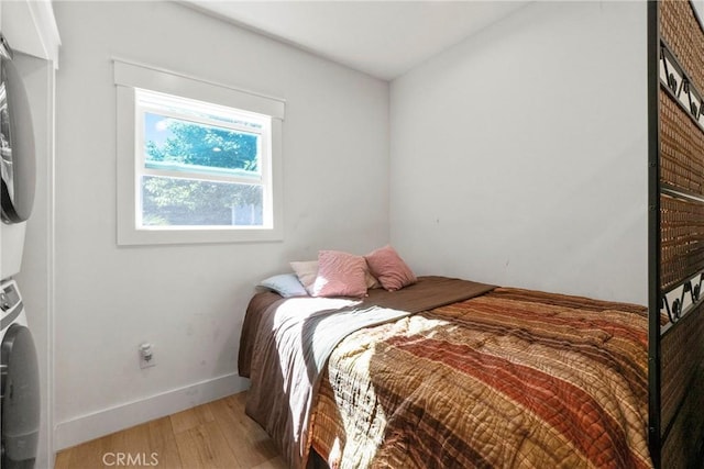 bedroom with hardwood / wood-style floors and stacked washing maching and dryer