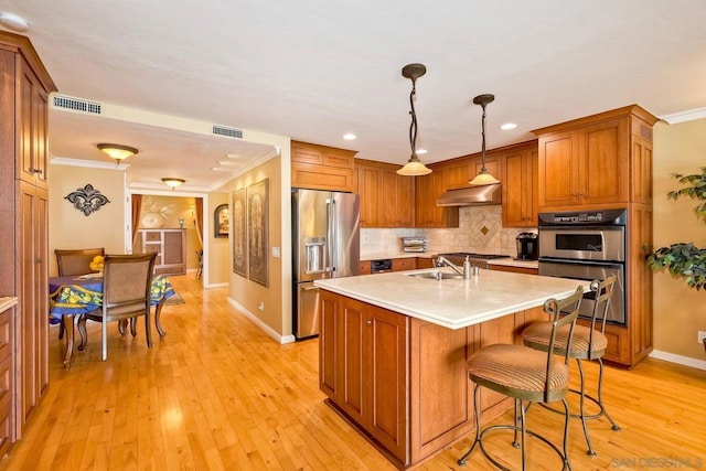 kitchen featuring appliances with stainless steel finishes, pendant lighting, sink, a center island with sink, and light hardwood / wood-style flooring