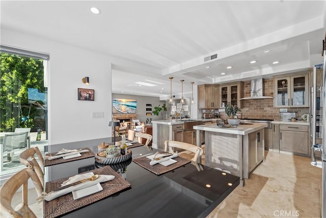 kitchen with a center island, hanging light fixtures, a raised ceiling, wall chimney range hood, and backsplash