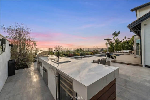 patio terrace at dusk featuring grilling area, beverage cooler, and an outdoor kitchen