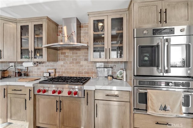 kitchen with appliances with stainless steel finishes, wall chimney exhaust hood, light brown cabinetry, and backsplash