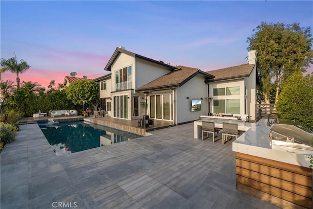 back house at dusk featuring a fenced in pool, exterior kitchen, and a patio