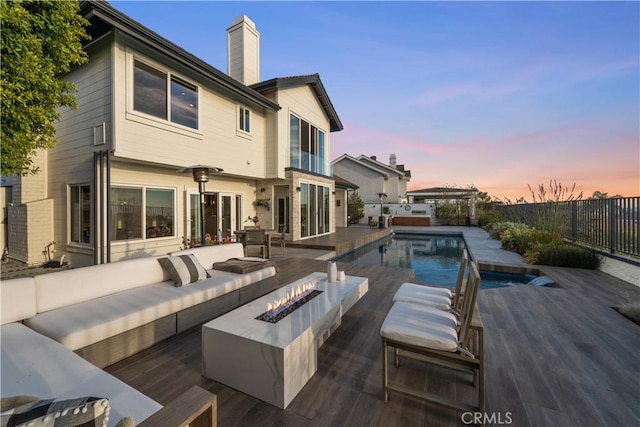 back house at dusk featuring a pool side deck and an outdoor living space with a fire pit