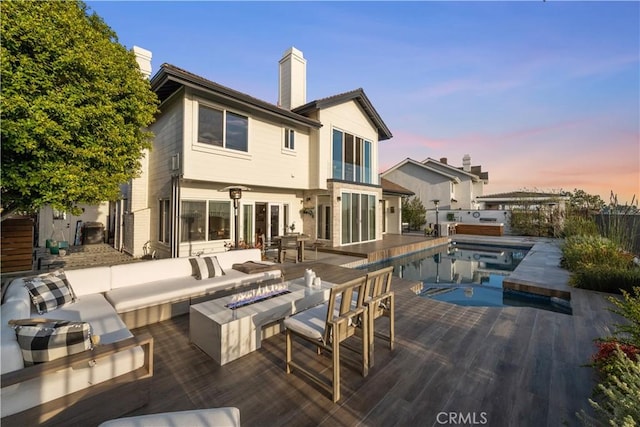 back house at dusk featuring a pool with hot tub and an outdoor living space with a fire pit