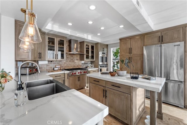 kitchen with wall chimney exhaust hood, stainless steel appliances, a tray ceiling, and pendant lighting