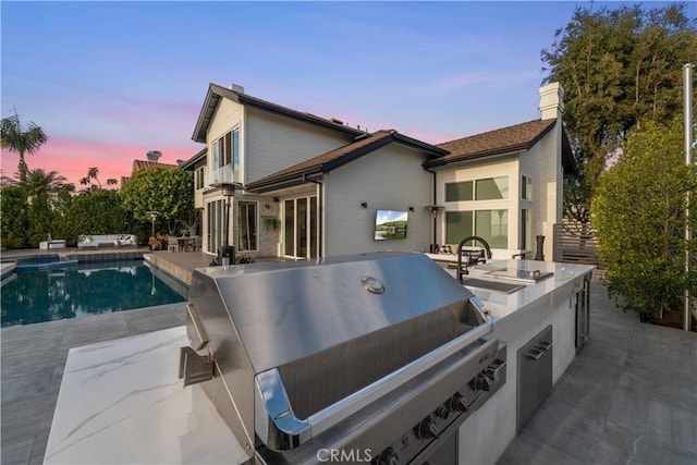 back house at dusk with a patio and exterior kitchen