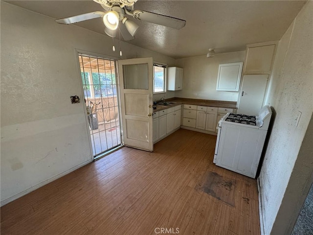 kitchen featuring white cabinetry, sink, ceiling fan, gas range gas stove, and light hardwood / wood-style flooring