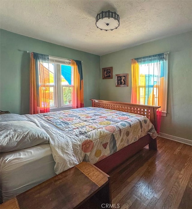 bedroom with multiple windows, a textured ceiling, baseboards, and wood finished floors