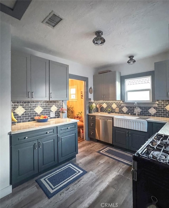 kitchen featuring dark wood-style flooring, visible vents, black range with gas stovetop, a sink, and dishwasher