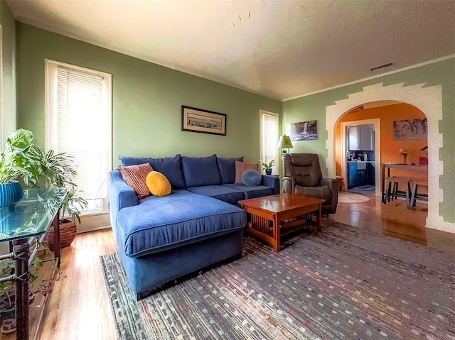 living area with visible vents, arched walkways, wood finished floors, a textured ceiling, and crown molding