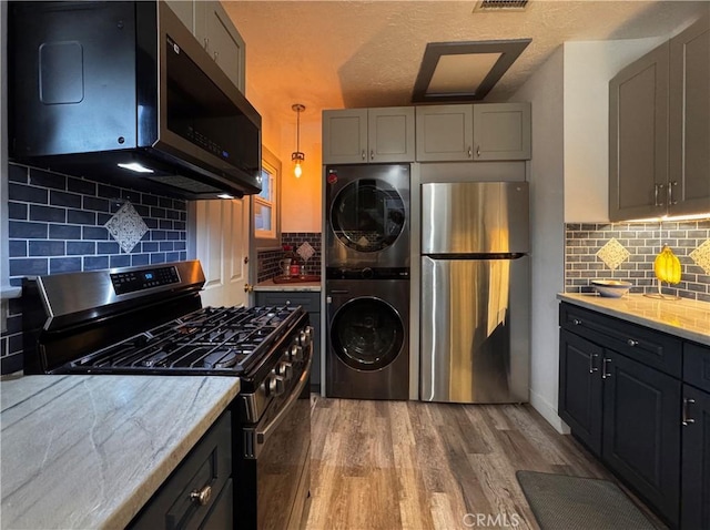 kitchen featuring light stone counters, gray cabinetry, stacked washer / drying machine, appliances with stainless steel finishes, and light wood finished floors