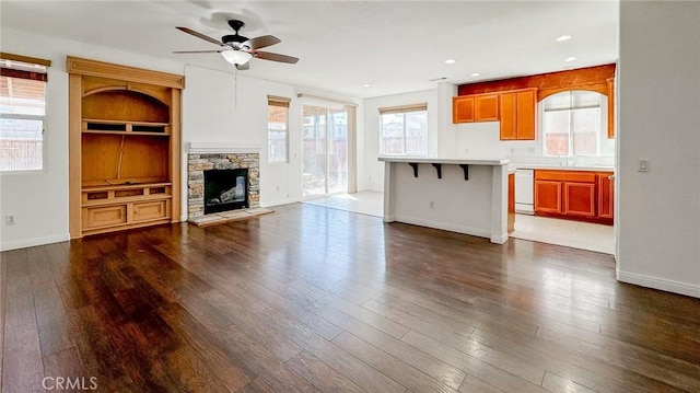 unfurnished living room with a stone fireplace, sink, dark hardwood / wood-style floors, built in features, and ceiling fan