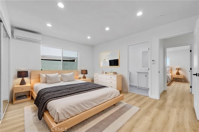 bedroom with a wall mounted air conditioner, ensuite bath, and light hardwood / wood-style flooring