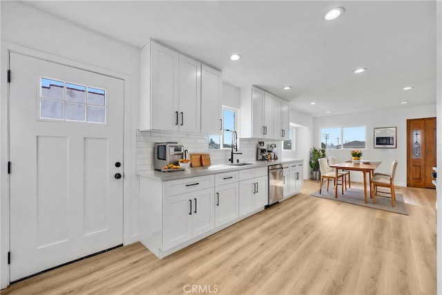 kitchen featuring tasteful backsplash, white cabinetry, sink, stainless steel dishwasher, and light hardwood / wood-style floors