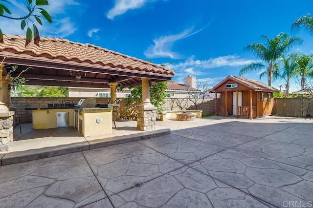 view of patio with a fire pit, a gazebo, a storage unit, area for grilling, and an outdoor kitchen