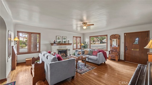 living room featuring a stone fireplace, hardwood / wood-style floors, and ceiling fan