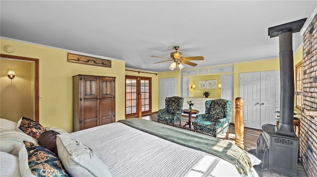 bedroom featuring wood-type flooring, a wood stove, ceiling fan, multiple closets, and french doors