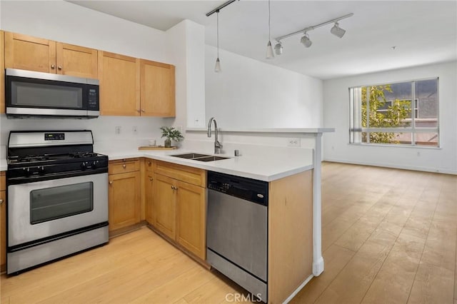 kitchen with sink, decorative light fixtures, light wood-type flooring, appliances with stainless steel finishes, and kitchen peninsula