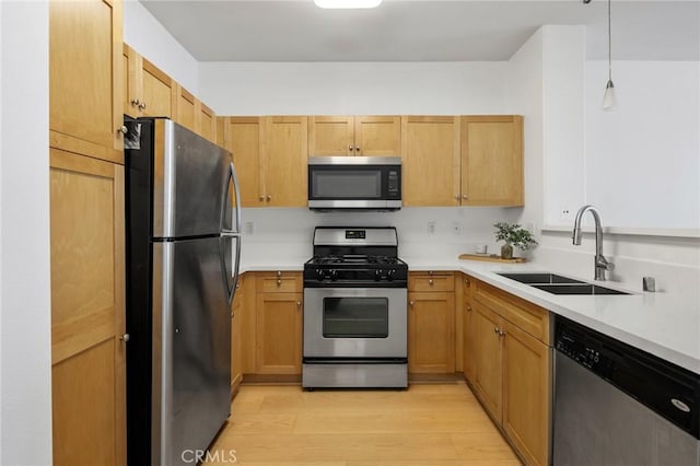 kitchen featuring sink, hanging light fixtures, stainless steel appliances, light brown cabinets, and light wood-type flooring