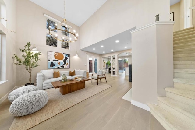 living room with an inviting chandelier, a towering ceiling, and light wood-type flooring