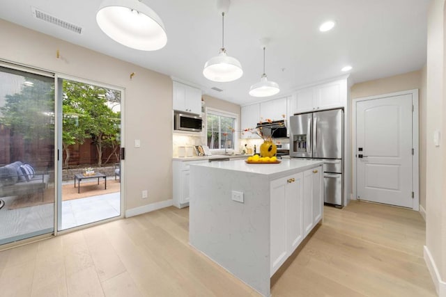 kitchen featuring light hardwood / wood-style flooring, appliances with stainless steel finishes, white cabinetry, hanging light fixtures, and a center island