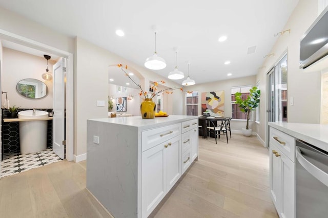 kitchen with light hardwood / wood-style flooring, white cabinetry, a center island, decorative light fixtures, and stainless steel dishwasher