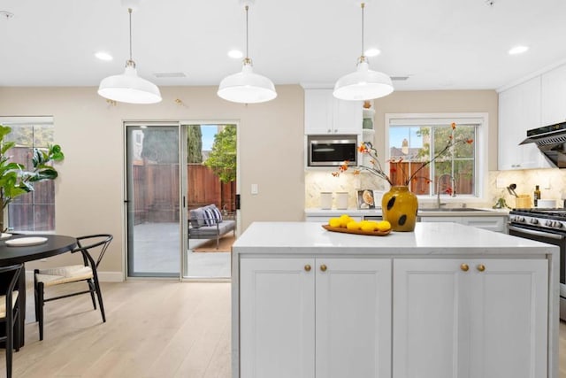 kitchen with sink, white cabinetry, stainless steel range with gas stovetop, a healthy amount of sunlight, and decorative light fixtures