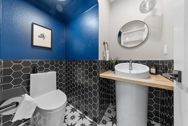 bathroom with toilet, sink, and tile walls