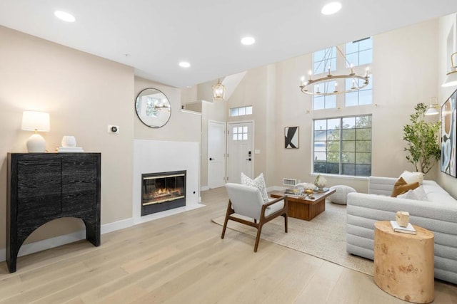 living room featuring a towering ceiling, an inviting chandelier, and light hardwood / wood-style flooring