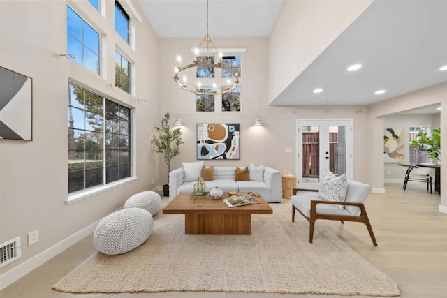 living room featuring french doors, a towering ceiling, light hardwood / wood-style flooring, and a notable chandelier