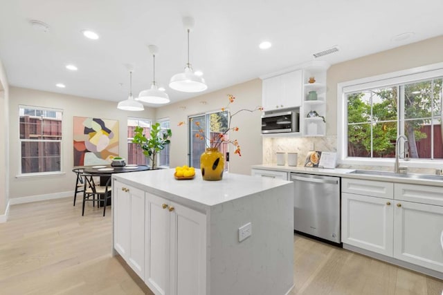 kitchen with appliances with stainless steel finishes, decorative light fixtures, white cabinetry, sink, and light hardwood / wood-style flooring