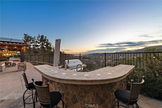 patio terrace at dusk featuring a bar and a grill