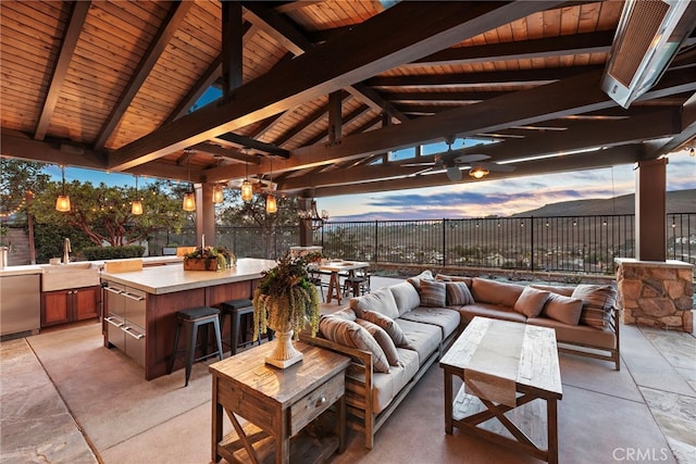 patio terrace at dusk with a gazebo, an outdoor hangout area, ceiling fan, and an outdoor wet bar