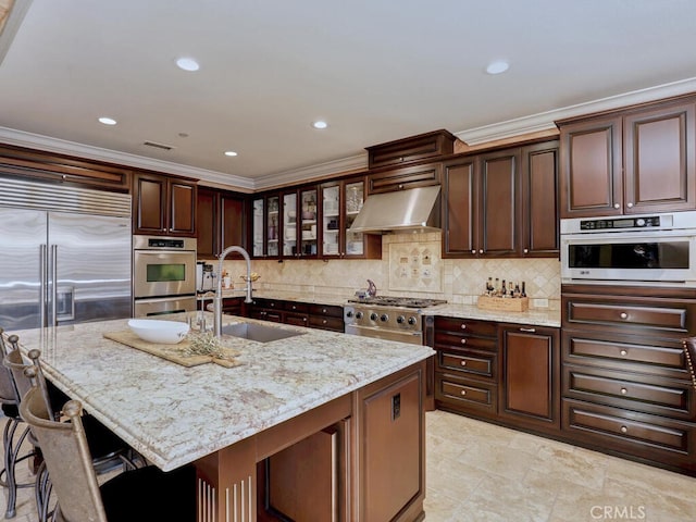 kitchen with extractor fan, an island with sink, sink, a kitchen breakfast bar, and light stone countertops