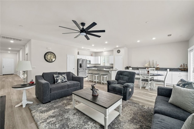 living room featuring light wood-type flooring, visible vents, ceiling fan, and recessed lighting