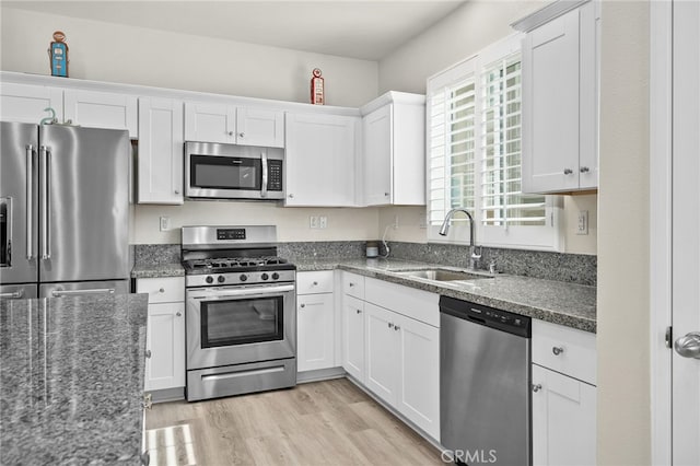 kitchen with a sink, dark stone countertops, light wood-style floors, appliances with stainless steel finishes, and white cabinets