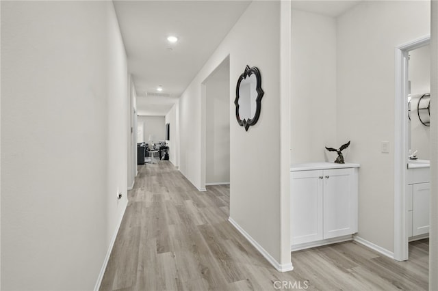 hall featuring visible vents, baseboards, recessed lighting, light wood-style floors, and a sink