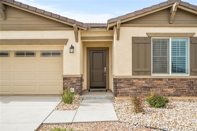 doorway to property featuring concrete driveway, a tile roof, stucco siding, a garage, and stone siding