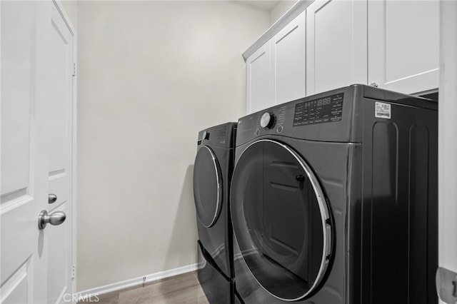 washroom featuring baseboards, cabinet space, wood finished floors, and washer and clothes dryer