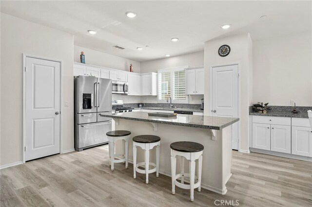 kitchen featuring visible vents, a center island, a breakfast bar, white cabinets, and stainless steel appliances