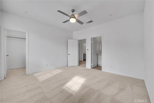 unfurnished bedroom with ensuite bathroom, a walk in closet, light colored carpet, ceiling fan, and a closet