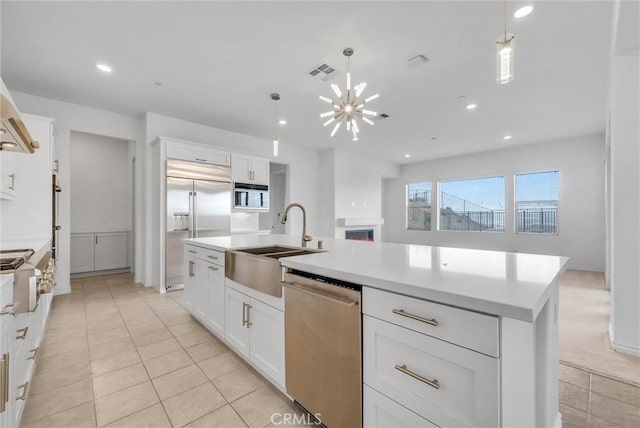 kitchen with sink, an island with sink, pendant lighting, stainless steel appliances, and white cabinets